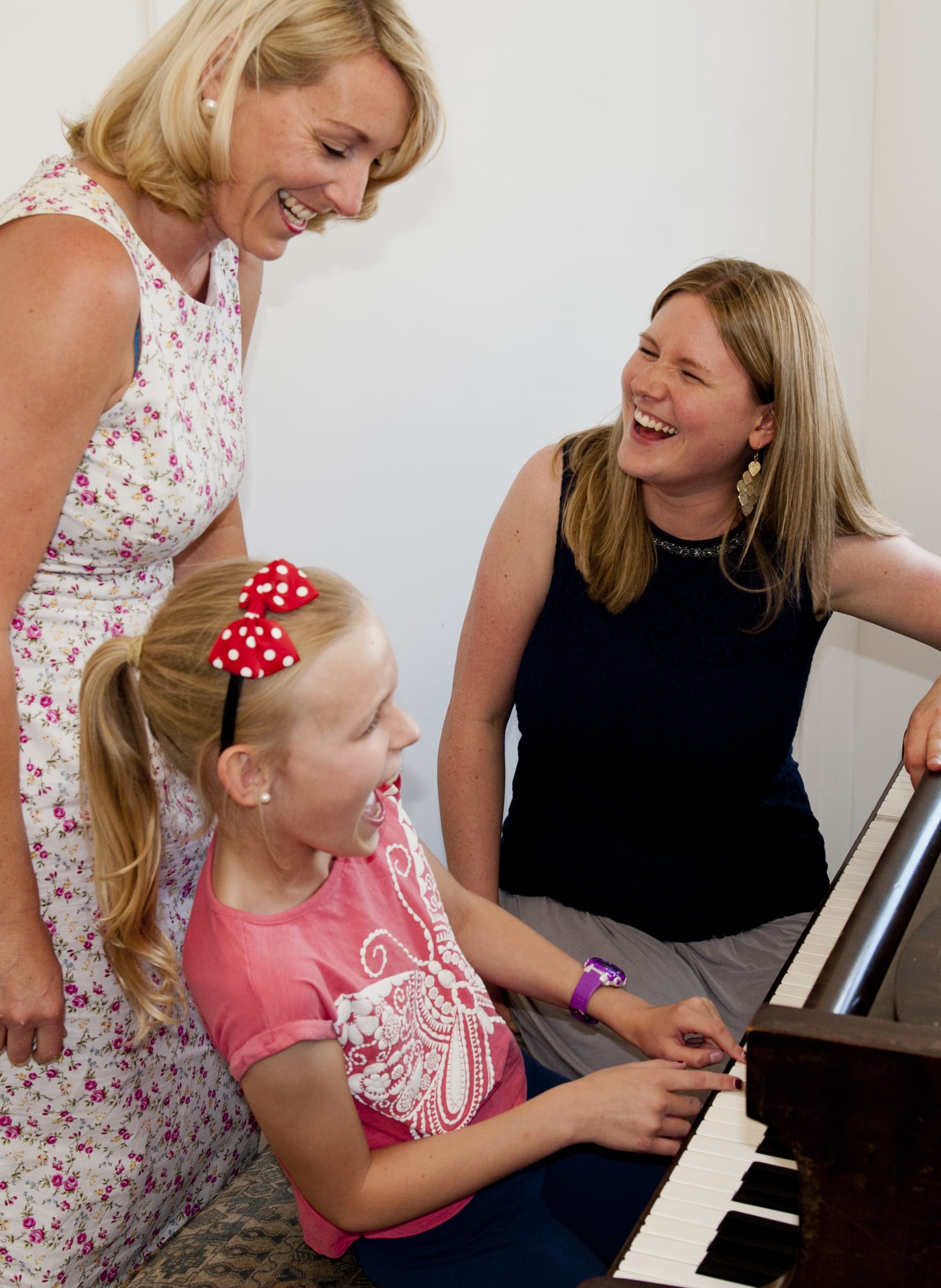 A piano lesson with child student and her mother and teacher playing piano together.