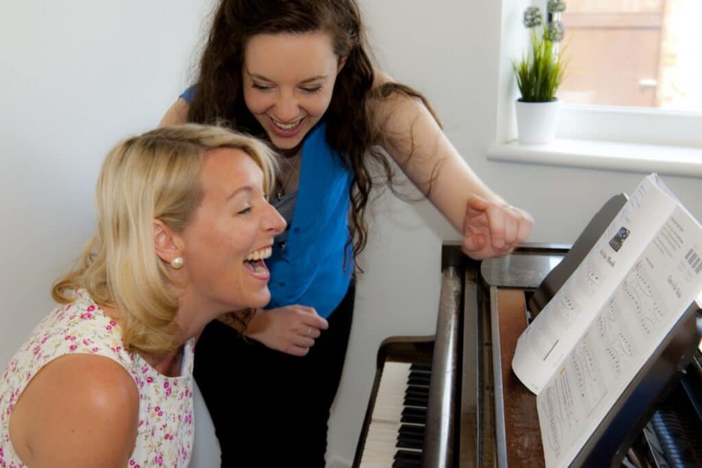 Adult blonde student laughs while learning piano with teacher